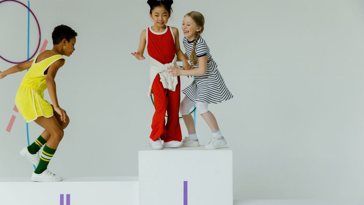Three children playing joyfully on a sports podium in a bright indoor setting.