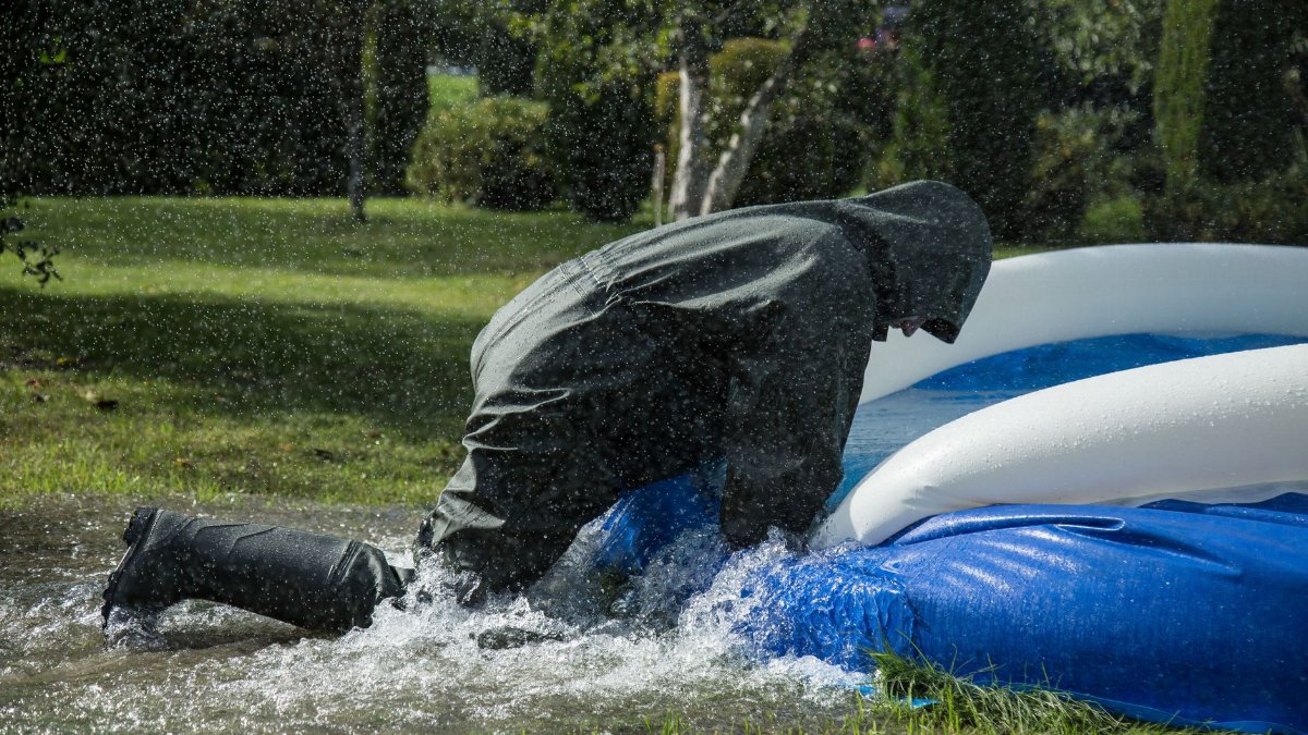 A person in rain gear leaning on an inflatable pool outdoors in wet conditions.