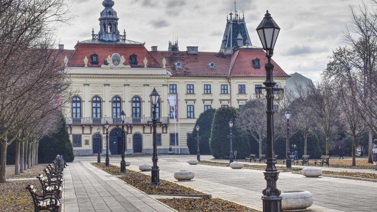 Elegant historic building with red roof and spires in a tranquil European city square.