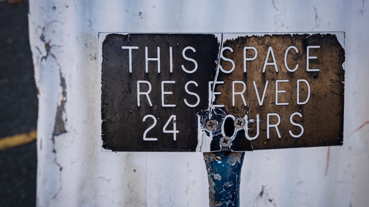 Rusted close-up of a weathered 'Reserved 24 Hours' parking sign in urban setting.
