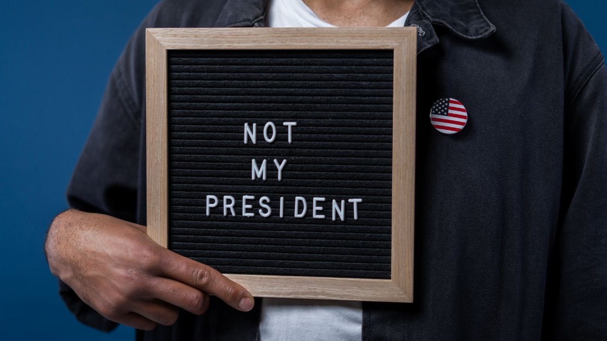 Person holding a letter board with 'Not My President' message and an American flag pin.
