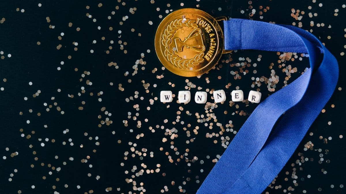 A gold medal with a blue ribbon on a black surface with glitter, symbolizing success.