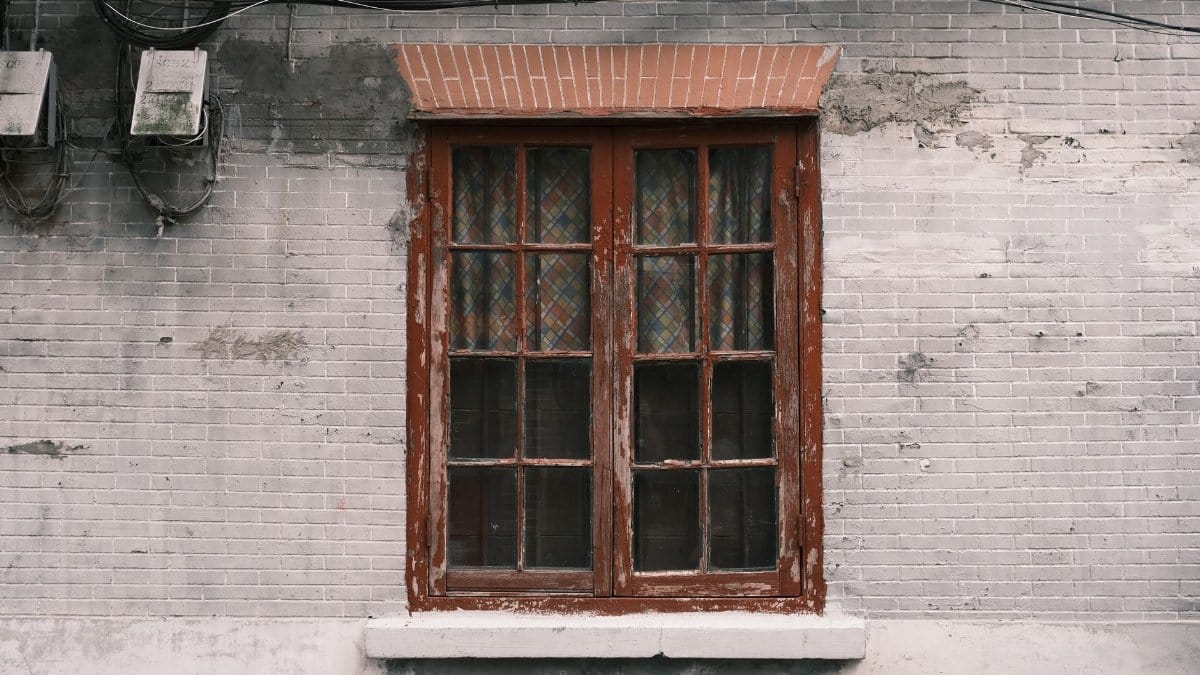 A vintage wooden window set in a worn, painted brick wall, capturing urban decay aesthetics.