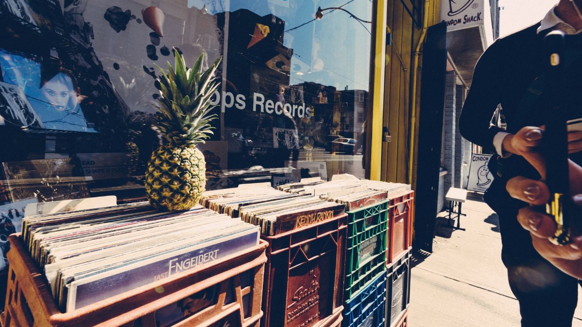 Street scene with a pineapple on record crates and a person using a smartphone.