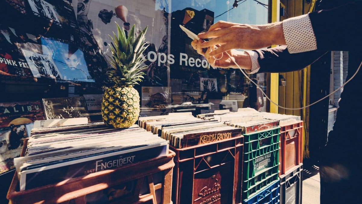 Man using a smartphone outside a record shop with vinyl crates and a pineapple. Urban lifestyle captured.