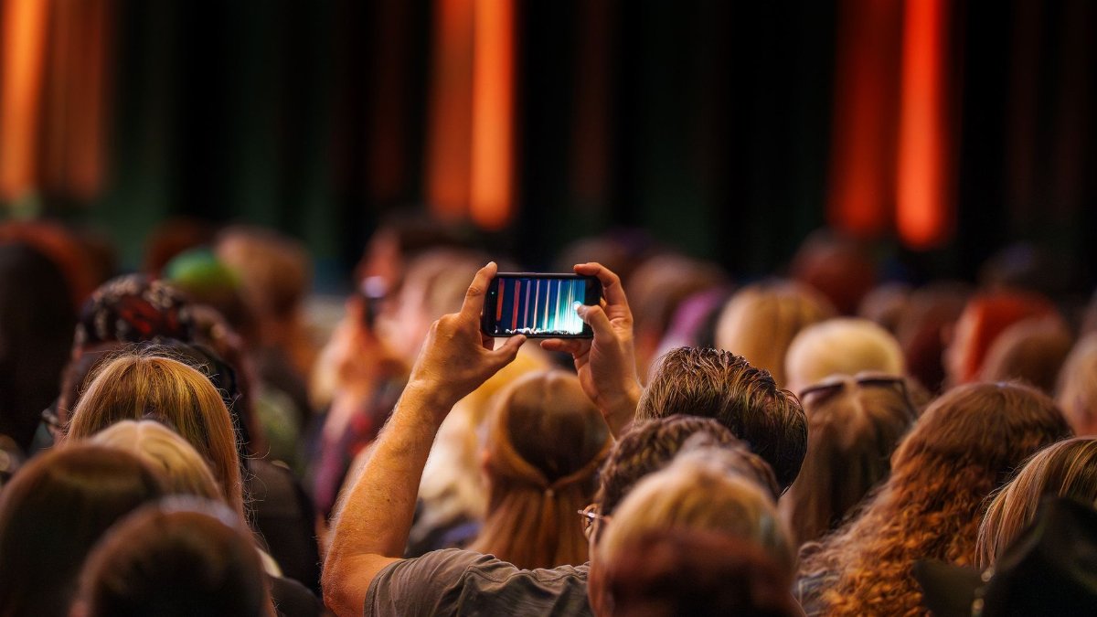 A crowd enjoys a live performance, recording on a smartphone at an indoor concert.