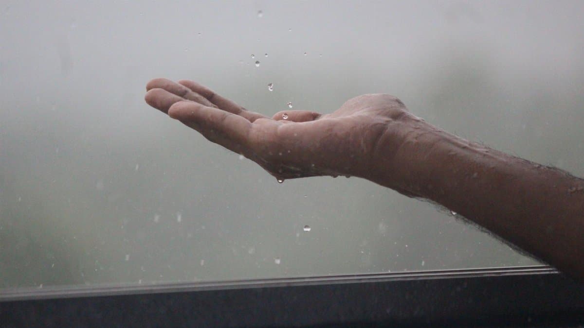Close-up of a hand reaching out to catch raindrops during a rain shower in Mangaluru, India.