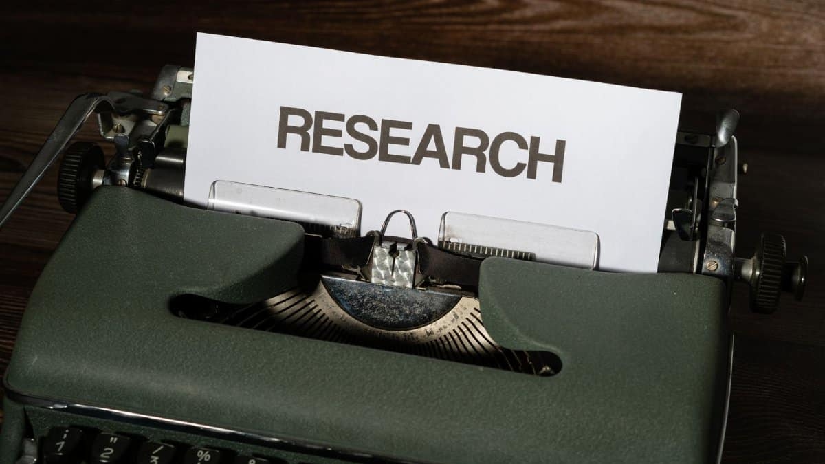 Close-up of a vintage typewriter with a paper labeled 'Research' inserted, on a wooden surface.