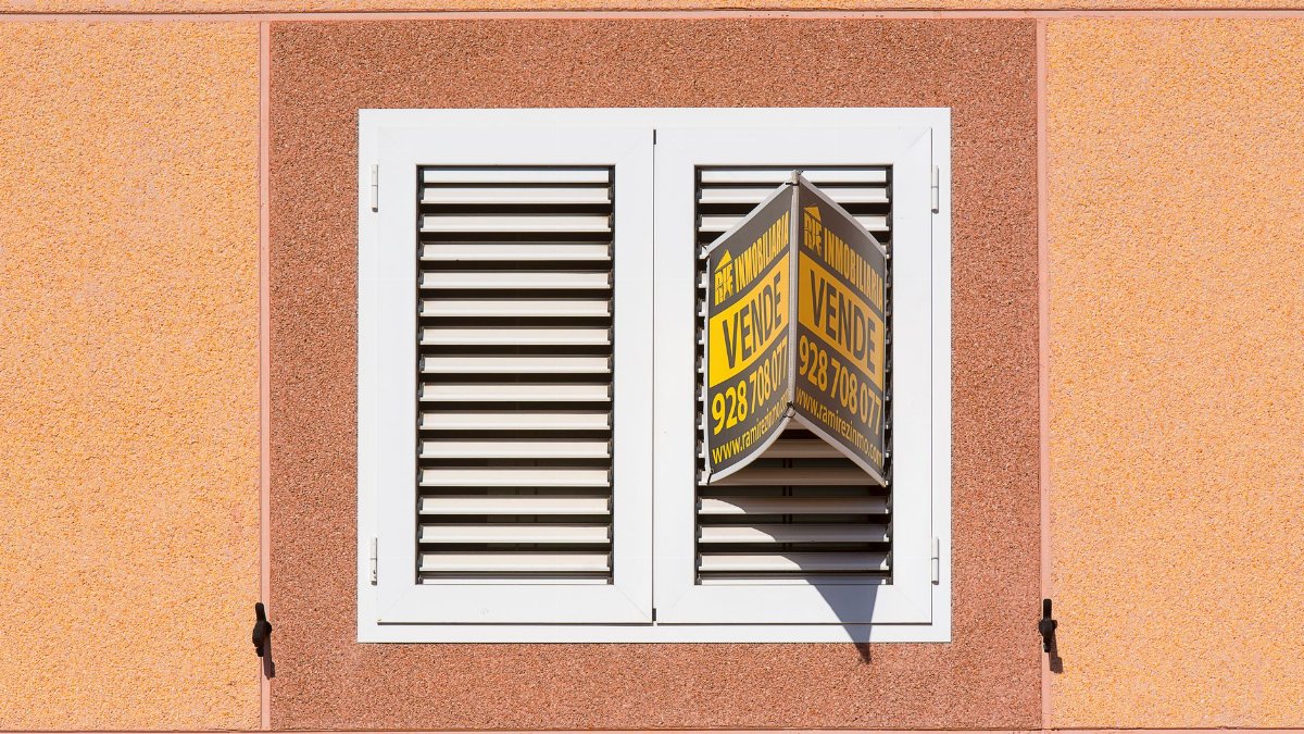 White shutter window with a for sale sign on peach building exterior.