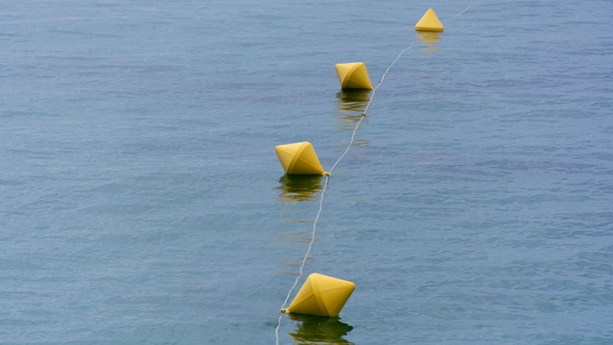 Geometric yellow buoys aligned in a line floating on calm ocean waters.