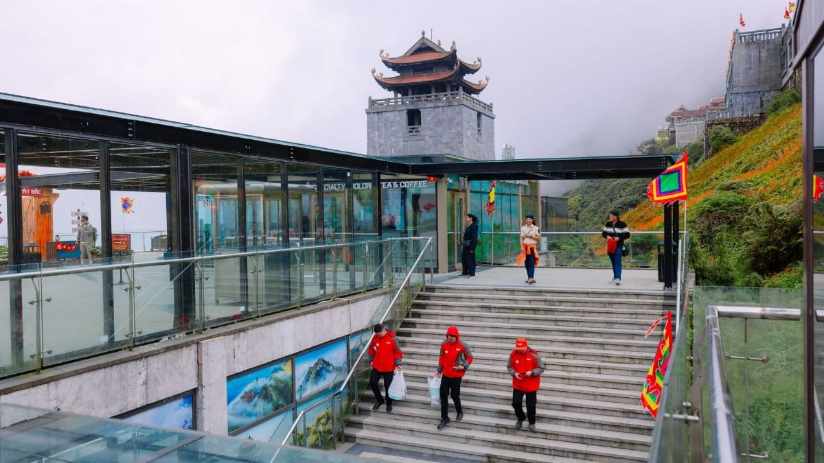 Visitors in red jackets approach a misty mountain temple in an Asian cultural setting.