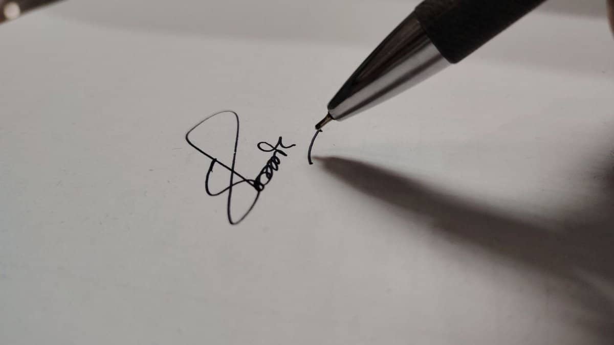 Macro shot of a pen writing a signature on white paper, emphasizing precision.