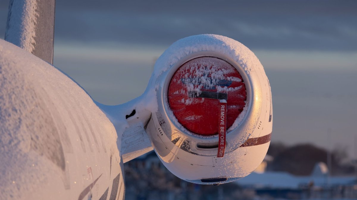 Airplane engine covered in snow at sunrise, showcasing winter aviation scene. Remove Before Flight tag visible.