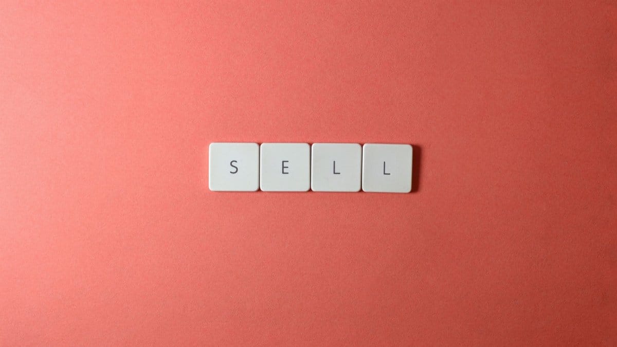 Close-up of keyboard tiles spelling 'sell' on a red background, minimalist design.