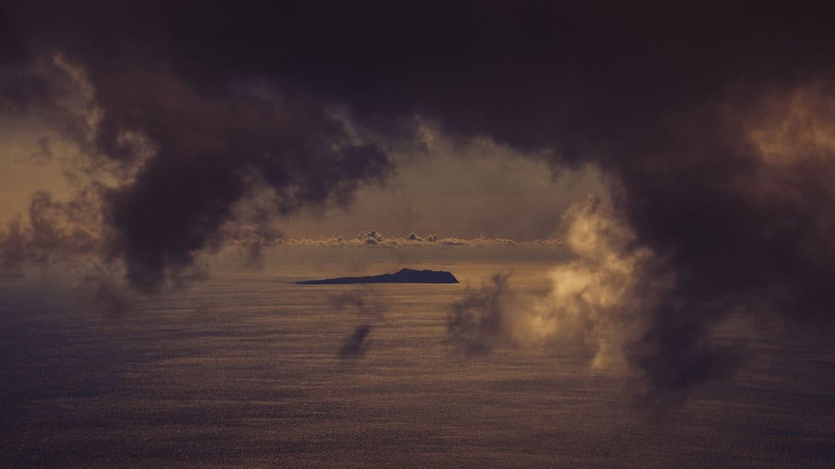 A lone island beneath dramatic storm clouds over the ocean, highlighting nature's power.