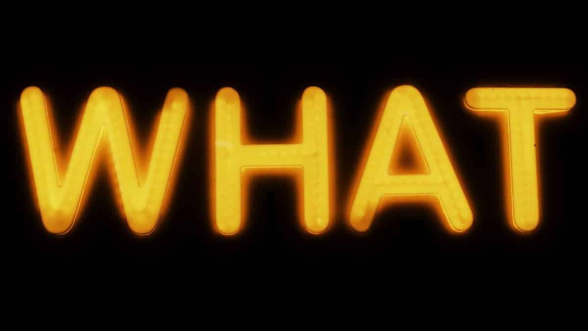 Bright yellow neon 'What' sign glowing against a black background in Budapest, Hungary.