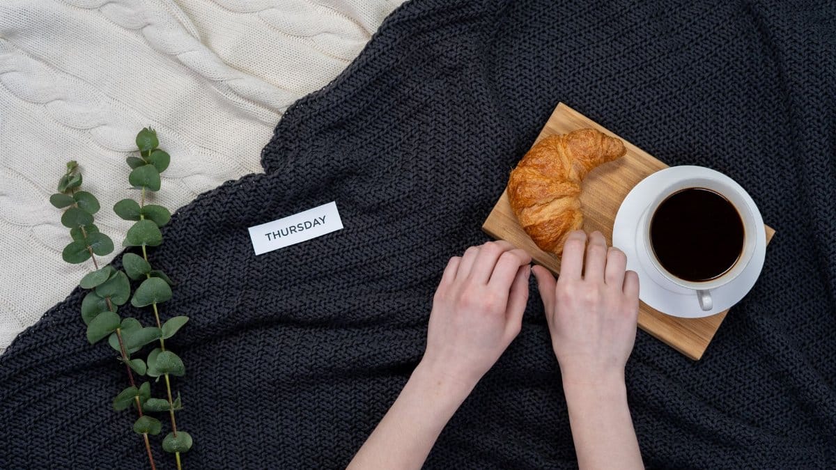 A relaxing setup with black coffee and croissant on a blanket, perfect for a cozy Thursday morning.