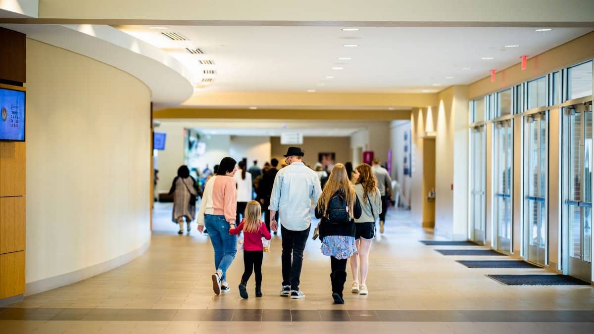 A family strolls through a bright, modern indoor corridor with large windows, creating a welcoming atmosphere.