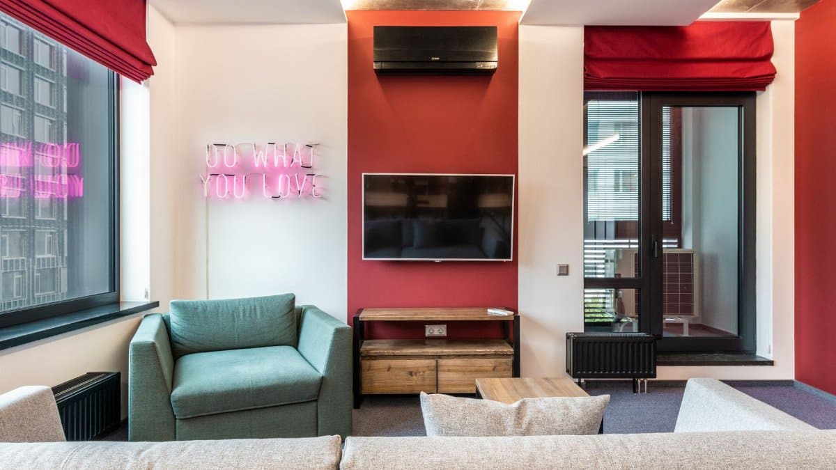 Interior of modern office lounge zone with sofa and armchair with table near window next to TV on wall and neon signboard with text do what you love near door
