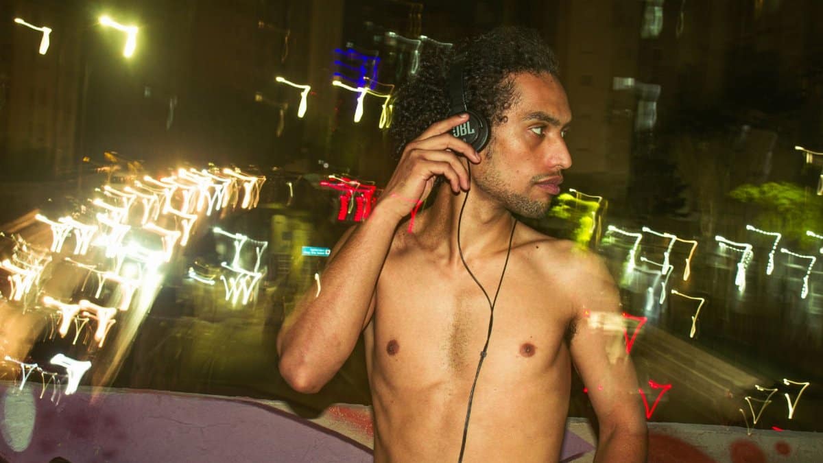 Shirtless man with headphones enjoying music in an urban night setting. Vibrant city lights create a dynamic background.