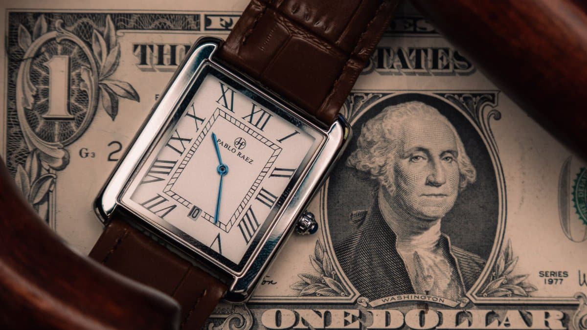 A classic watch placed on a US dollar bill, symbolizing time and money.