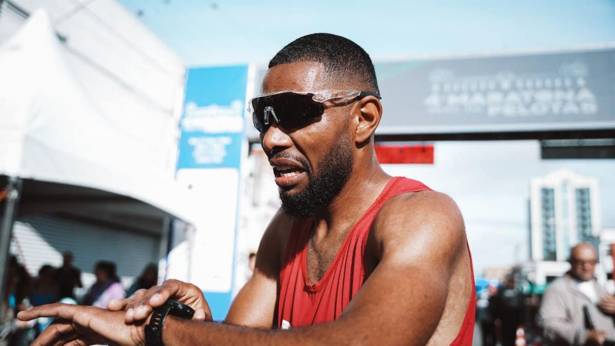 A marathon runner checks his time at the finish line after a race, wearing sunglasses and a smartwatch.