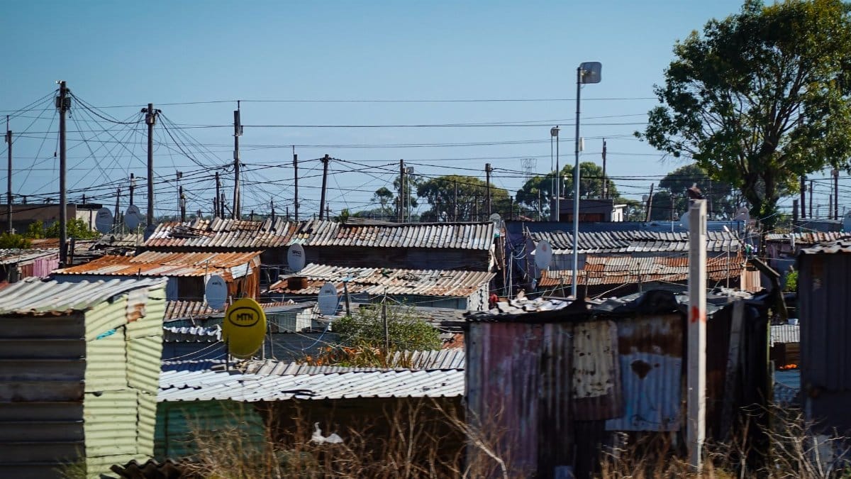 A view of an informal settlement with numerous makeshift rooftops and power lines.