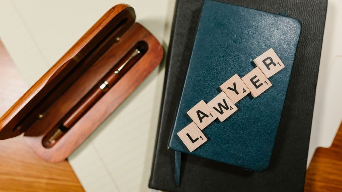 Scrabble tiles spelling 'LAWYER' on a blue notebook with a wooden pen case, overhead view.