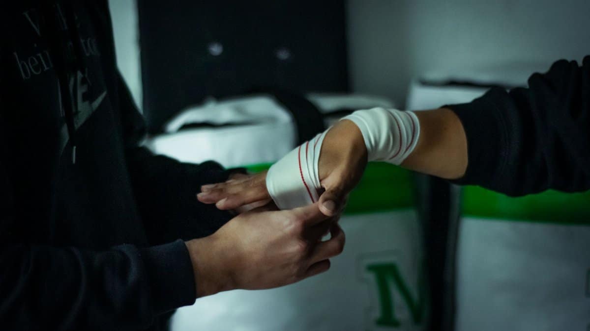 Close-up of a boxer's hands being wrapped with tape in a gym setting, highlighting preparation and focus.
