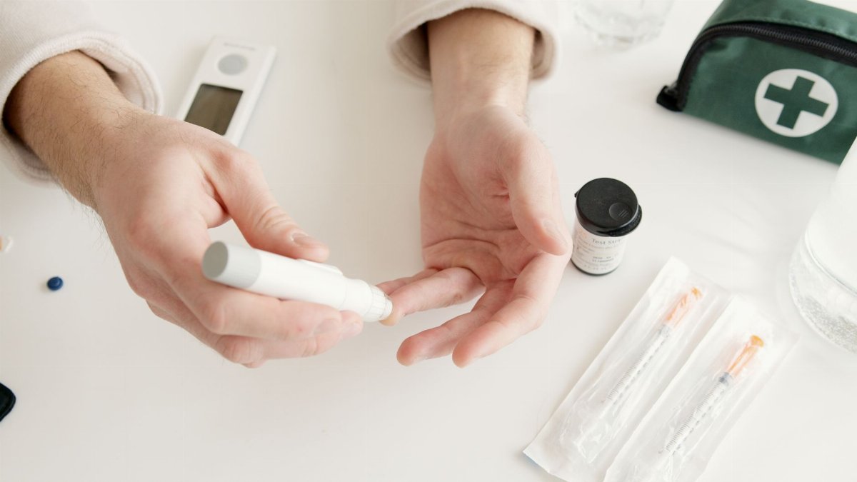 Hands using a glucometer to test blood sugar, with a medical kit and syringes visible nearby.