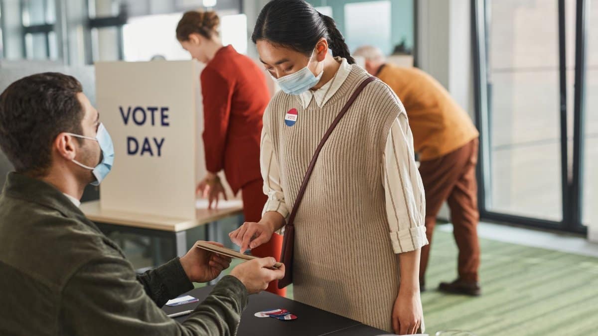 Voters casting ballots indoors on Election Day, wearing masks and using tablets for contactless voting.