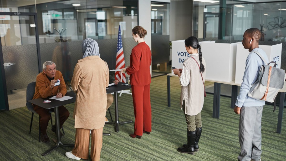 Diverse group of voters lining up at an indoor polling station on election day.