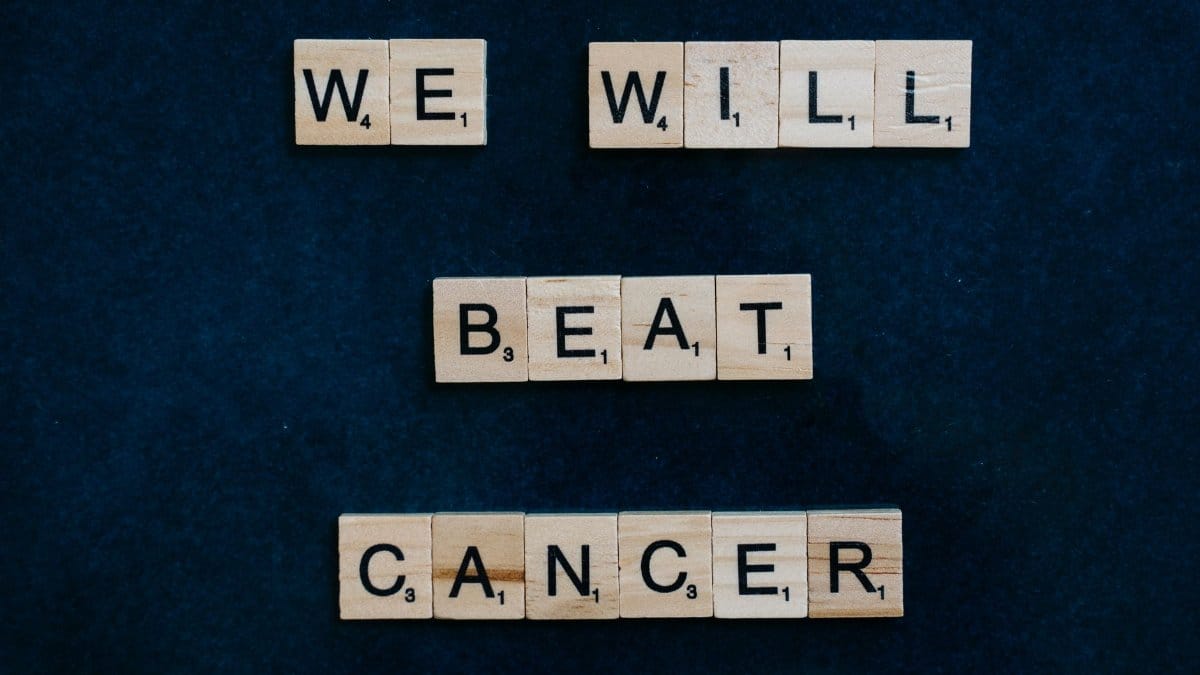 Motivational message 'We Will Beat Cancer' spelled out with Scrabble tiles on a dark background.