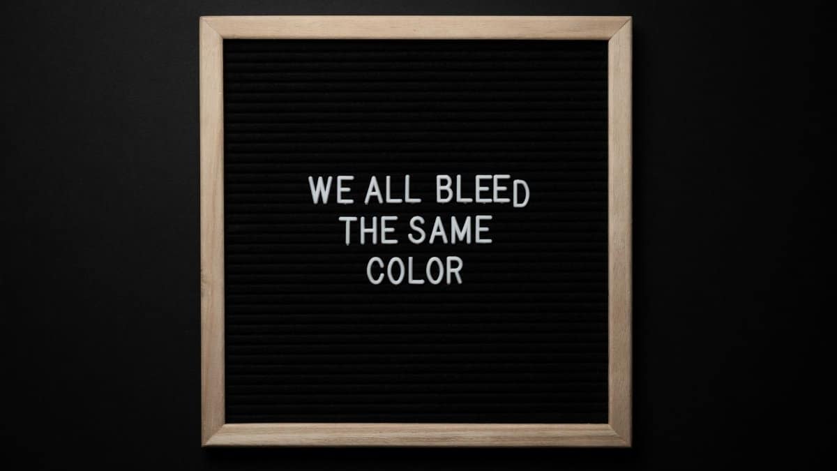 Top view of black signboard with phrase We All Bleed Same Color on surface on black background