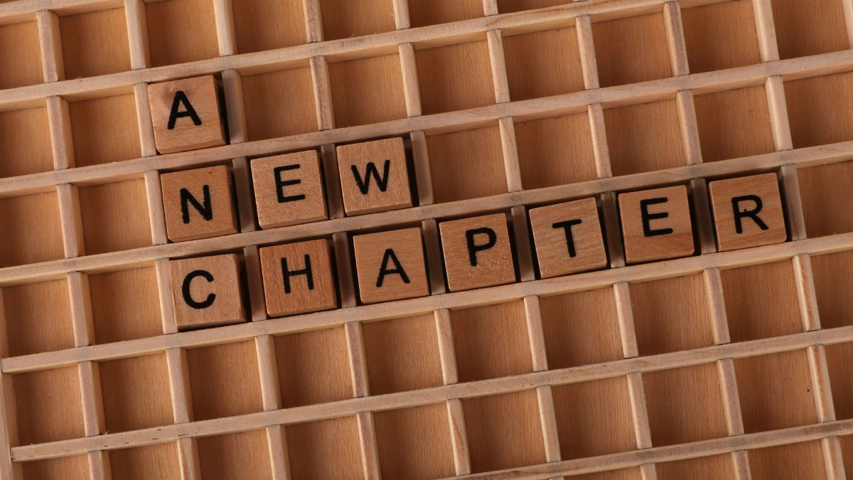 Wooden Scrabble letters arranged to spell 'A New Chapter' on a gridded board.