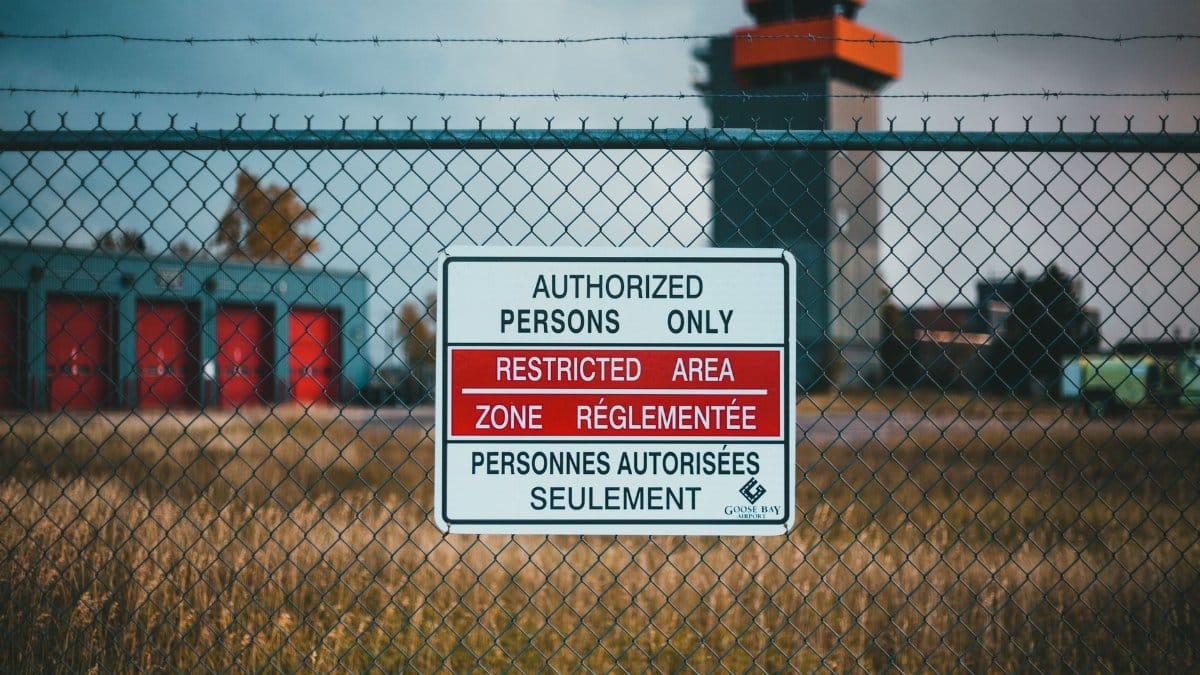 A close-up of a restricted area sign on a barbed wire fence outside an industrial area.