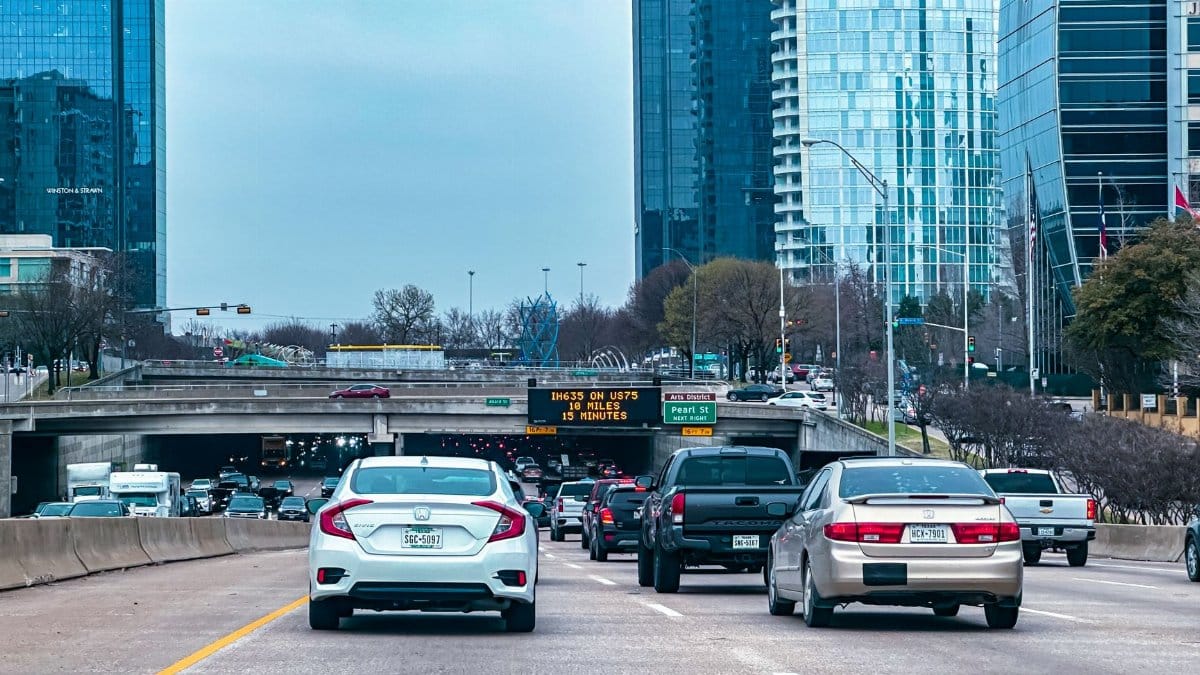 Busy traffic scene on a Dallas highway with skyscrapers in the background.