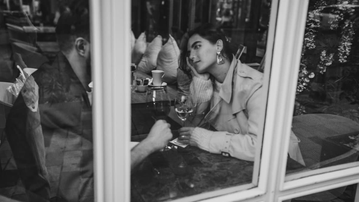 Black and white image of a couple enjoying a romantic date with wine by a window.