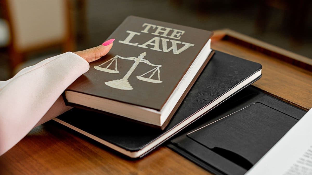 Closeup image of a law book titled 'The Law' on a wooden desk with scales of justice.