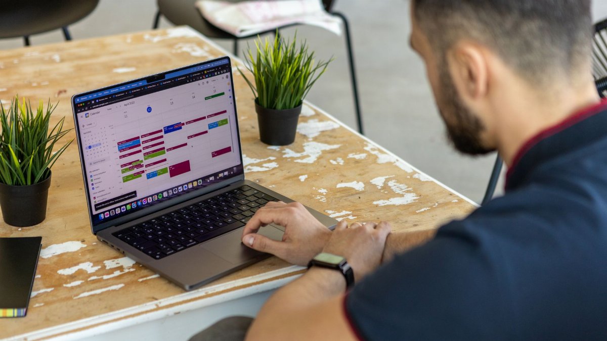 Man working remotely at a desk with a laptop open to a calendar app.