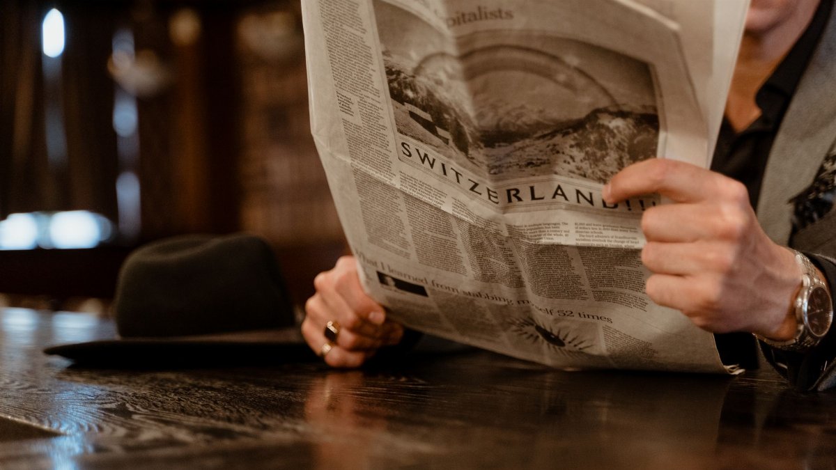 Close-up of man reading newspaper with focus on Switzerland headline.