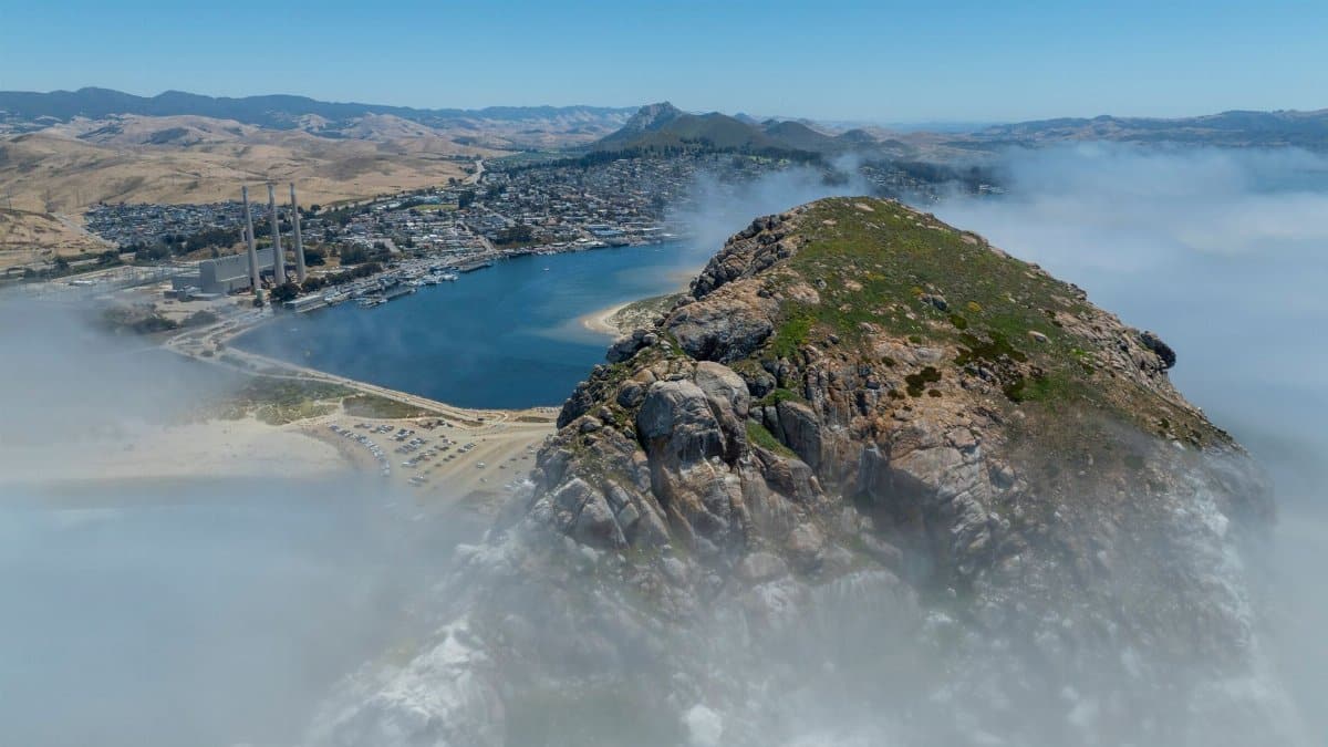 A stunning aerial view of Morro Bay, CA, enveloped in fog with its iconic rock formation.