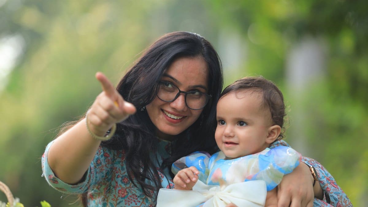 A candid outdoor photo of a mother and baby enjoying a first birthday celebration.