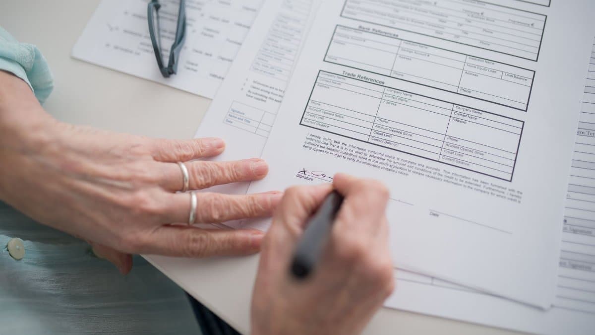 A close-up view of a hand signing official documents with a pen indoors.