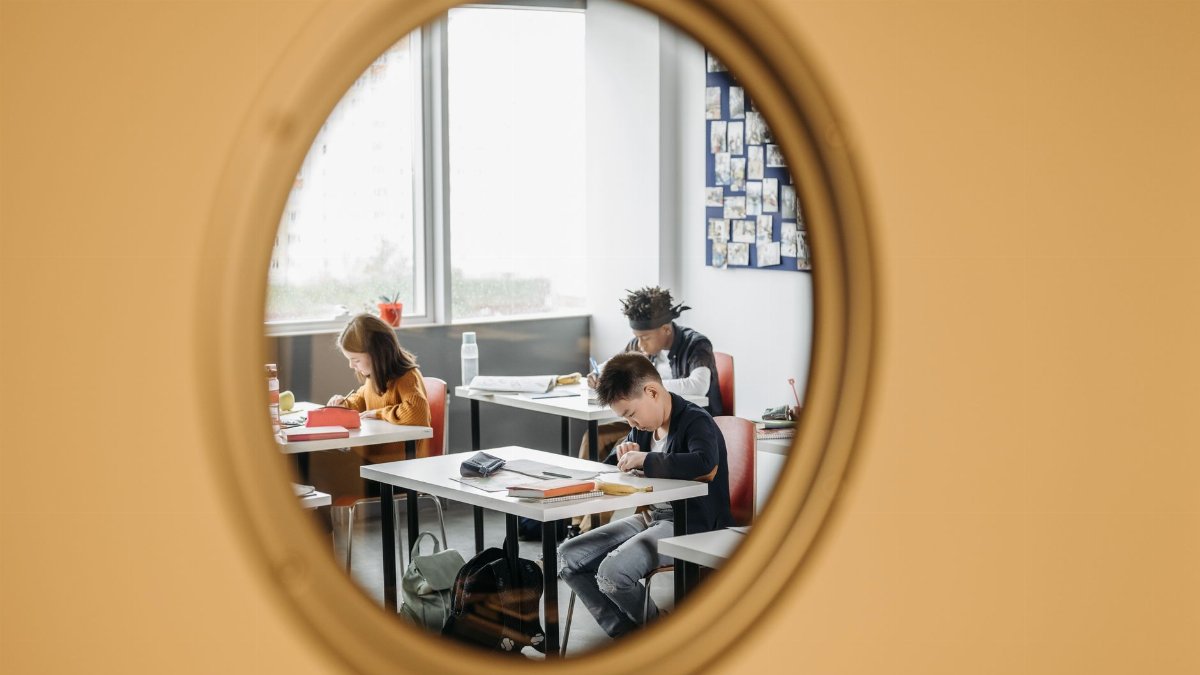 Three students focusing on studies in a classroom, viewed through a round window.