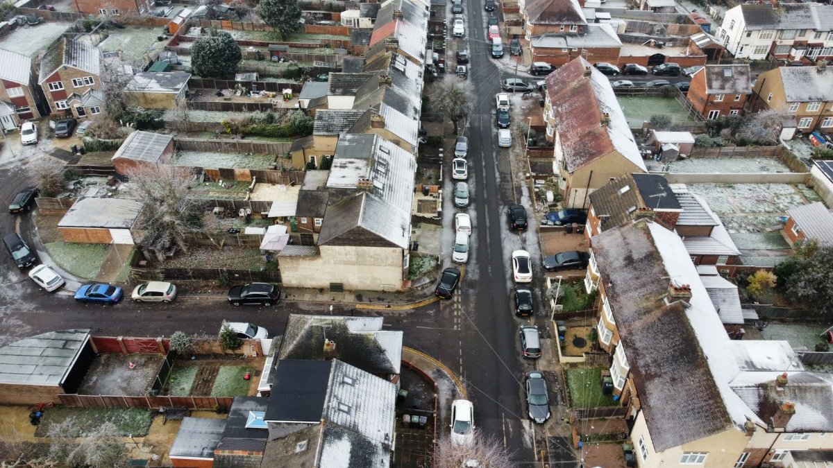 Drone shot of a winter residential area with snow on rooftops and parked cars lining the streets.