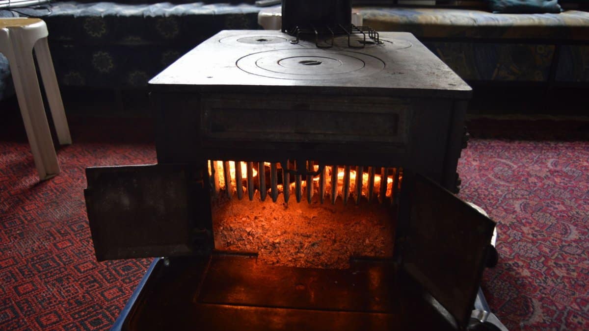 A classic vintage wood heater radiating warmth in a cozy, carpeted interior room.