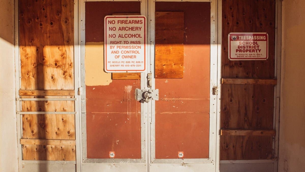 A locked and boarded school entrance with no trespassing signs emphasizing safety rules.