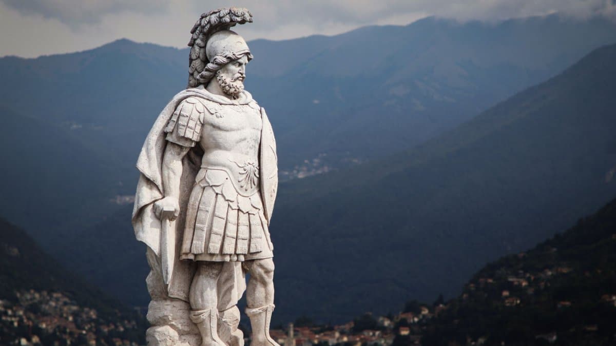 Majestic warrior statue overlooking the serene Lake Como with mountain backdrop.