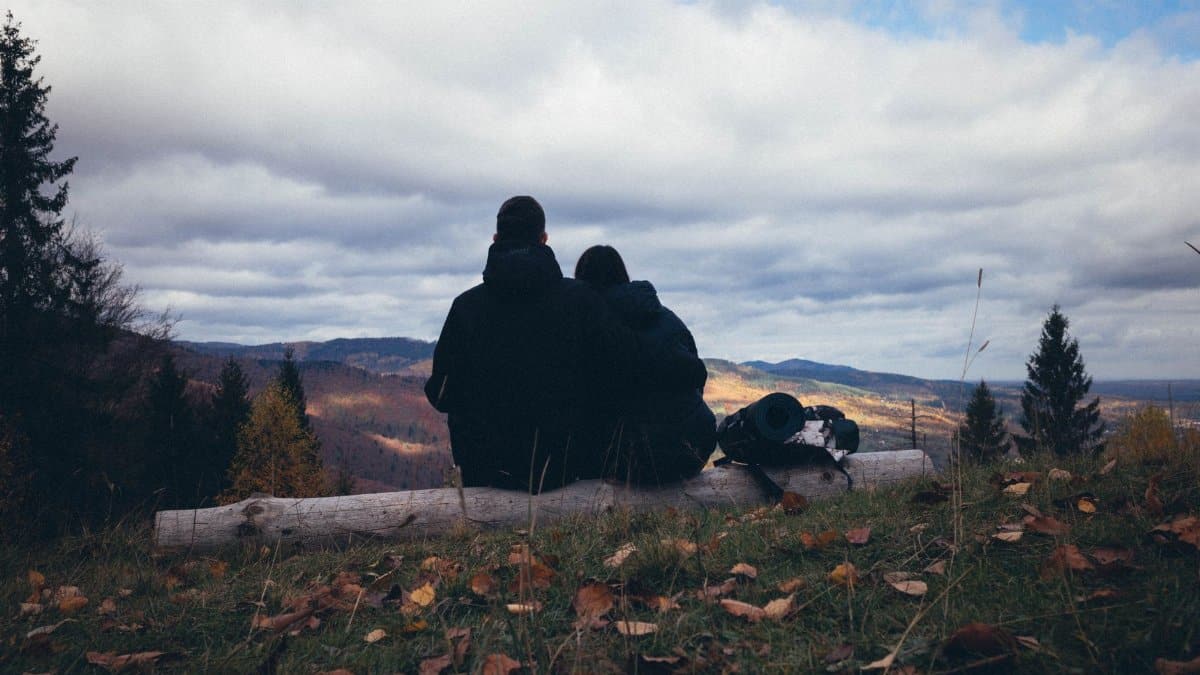 A couple sits on a log, enjoying a peaceful mountain view during autumn.